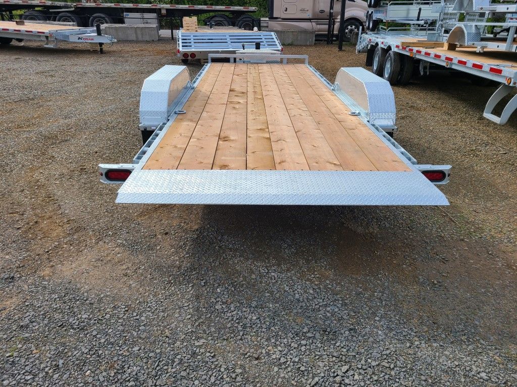 Une remorque avec une terrasse en bois est garée sur un terrain en gravier.