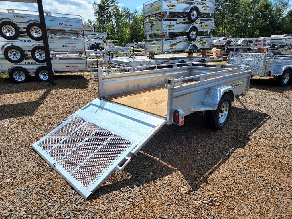 Une remorque est garée sur un terrain en gravier à côté d'une pile de remorques.