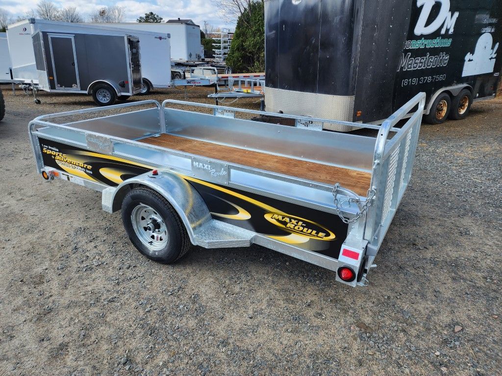 Une remorque avec une terrasse en bois est garée sur un terrain en gravier.