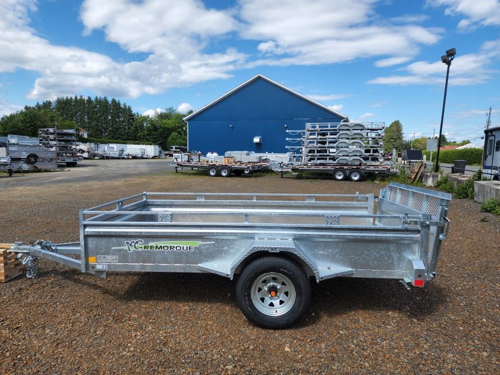 Une remorque est garée sur un terrain en gravier devant un bâtiment bleu.