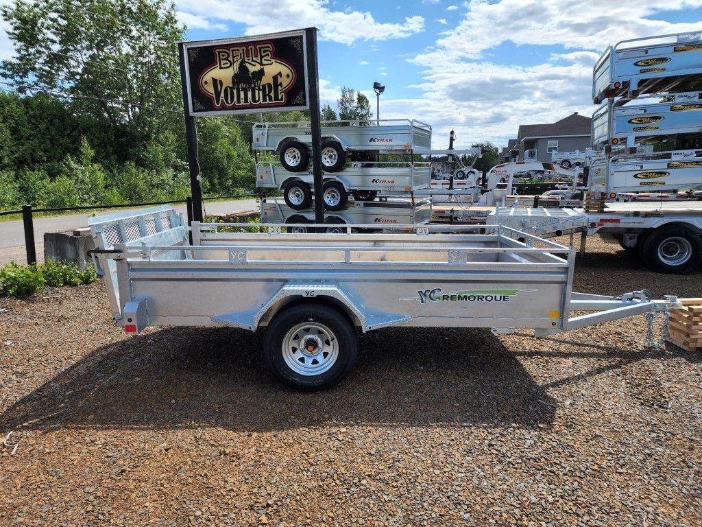 Une remorque est garée sur un terrain en gravier à côté d'un panneau.