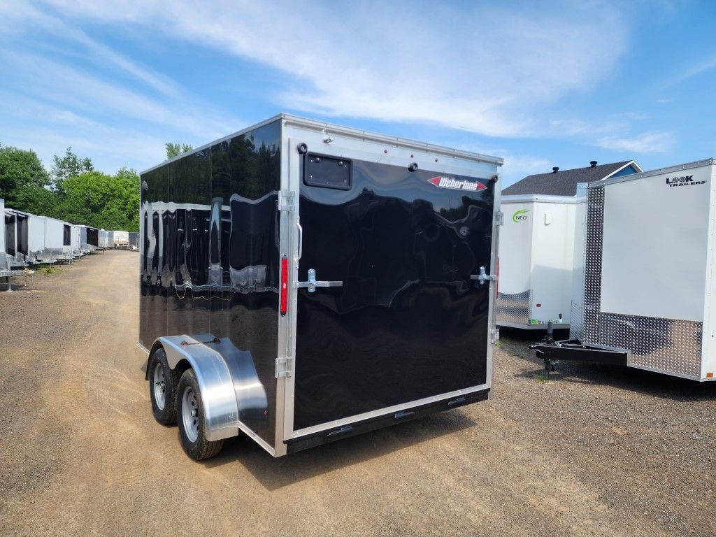 Une remorque noire est garée sur un terrain en terre.