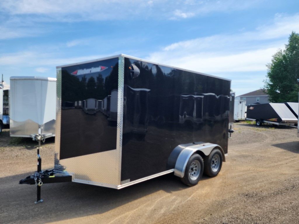 Une remorque noire est garée sur un terrain en terre.