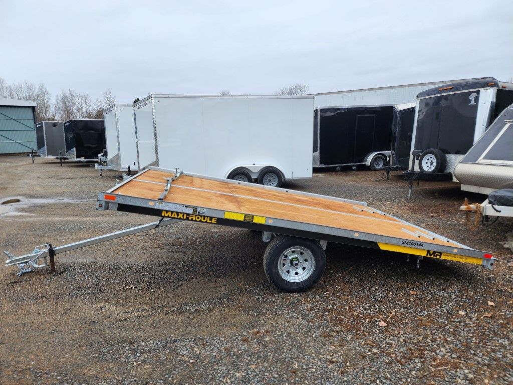 Une remorque à plateau est garée sur un terrain en gravier.