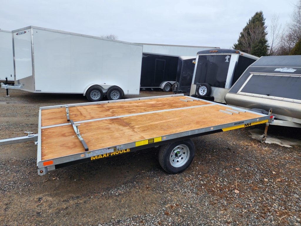 Une remorque à plateau est garée sur un terrain en gravier.