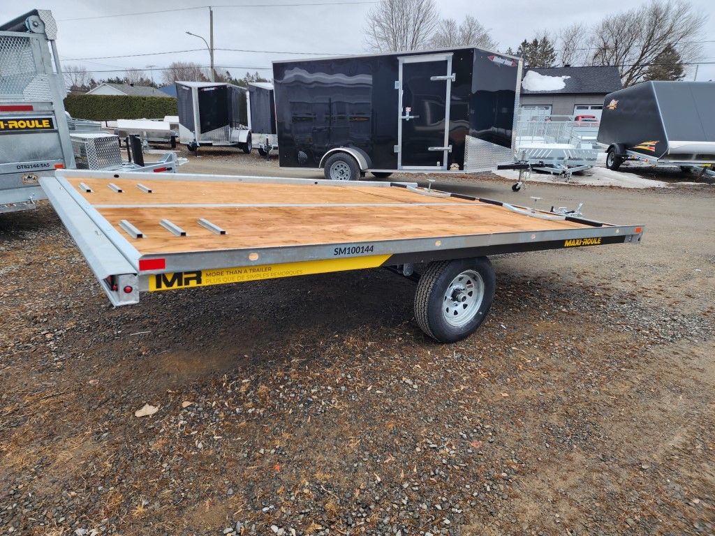 Une remorque de moto est garée sur un terrain en gravier.