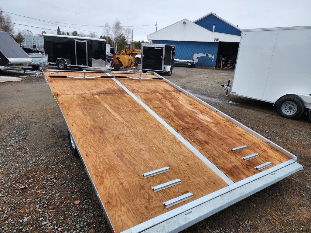 Une remorque en bois est garée sur un terrain en gravier à côté d'une remorque blanche.