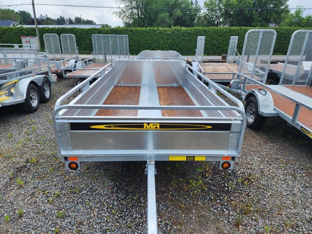 Une remorque avec le mot M. dessus est garée sur un terrain en gravier.