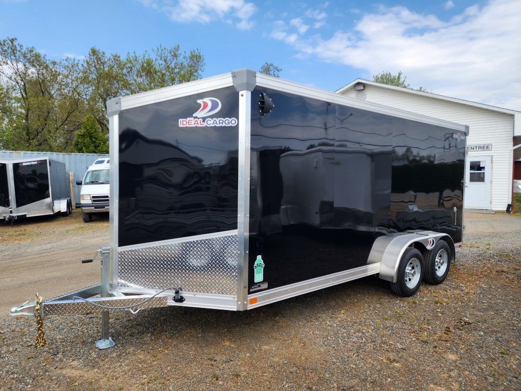 Une remorque noire est garée sur un terrain en gravier devant un bâtiment.