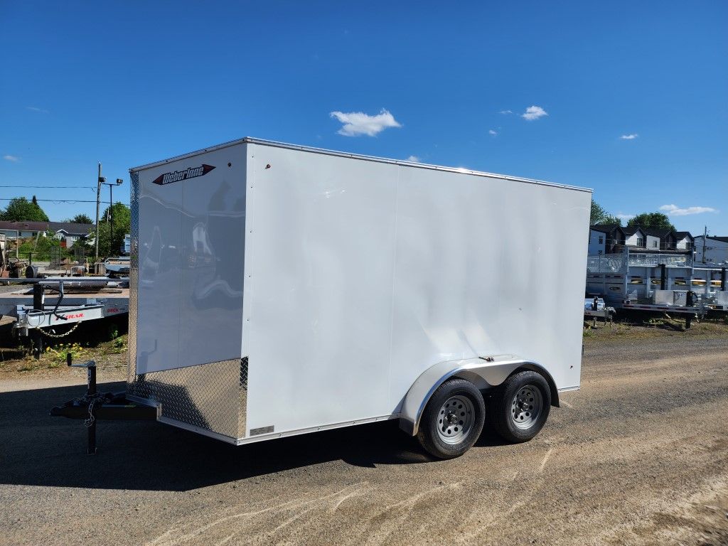Une remorque blanche est garée sur le bord d'un chemin de terre.