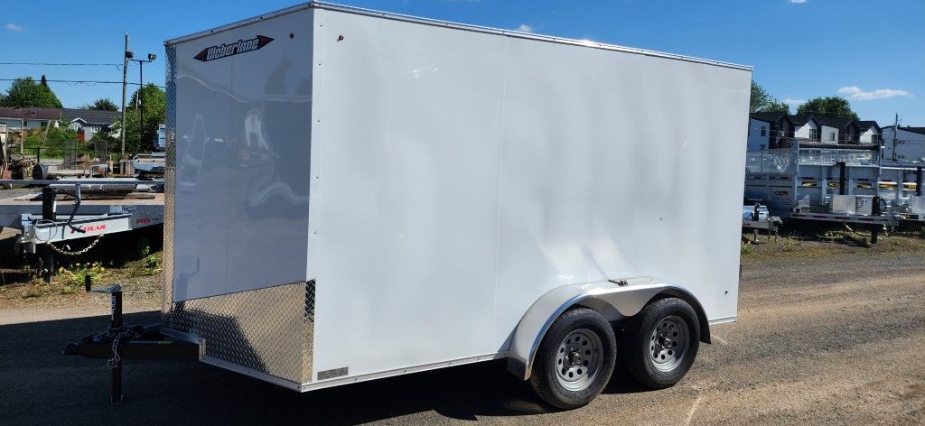 Une remorque blanche est garée sur le bord d'un chemin de terre.