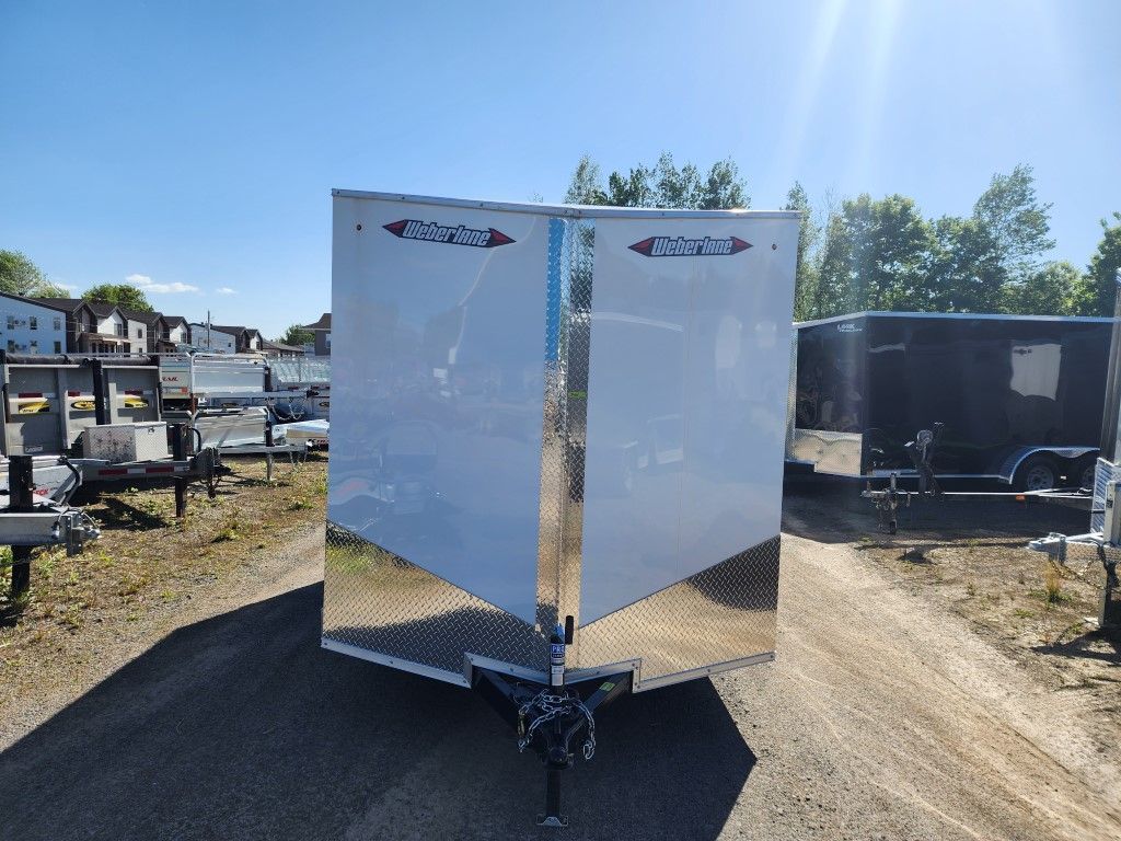 Une remorque blanche est garée sur le bord d'un chemin de terre.