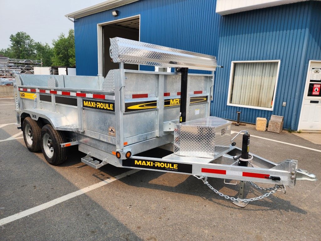 Une remorque à benne basculante est garée devant un bâtiment bleu.