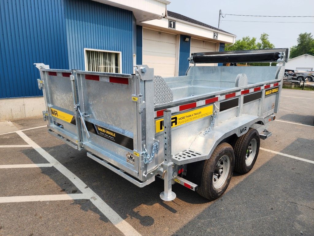 Une remorque à benne basculante est garée sur un parking devant un bâtiment.