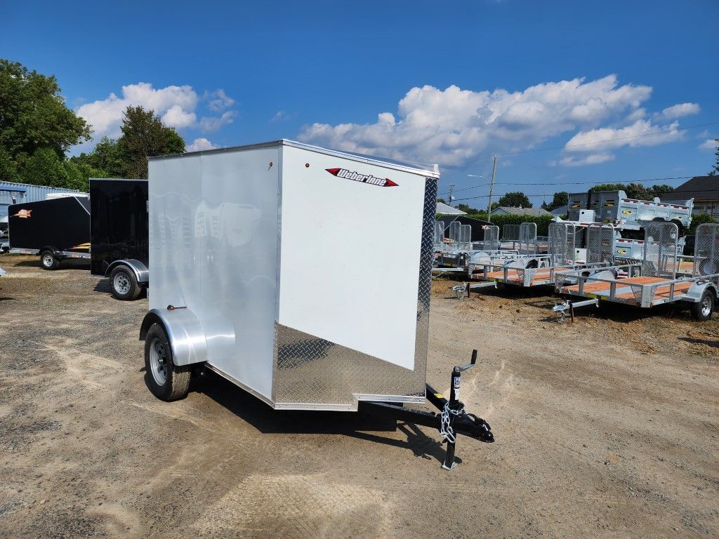 Une remorque blanche est garée sur un terrain en terre.