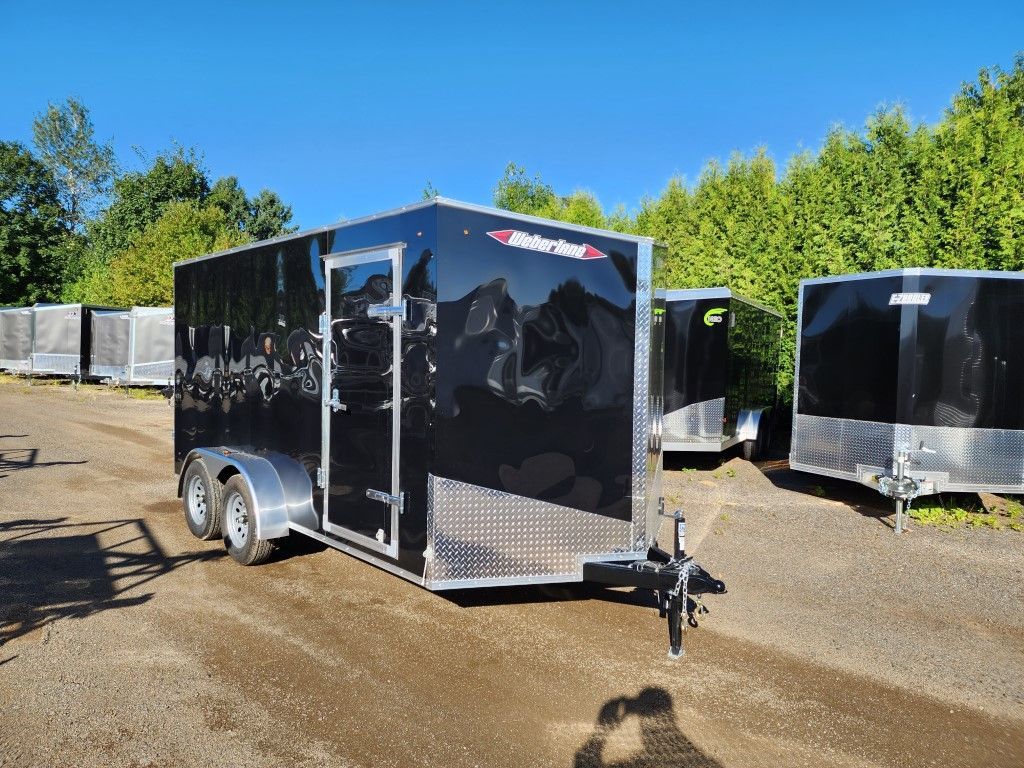 Une remorque noire est garée sur un terrain en terre.