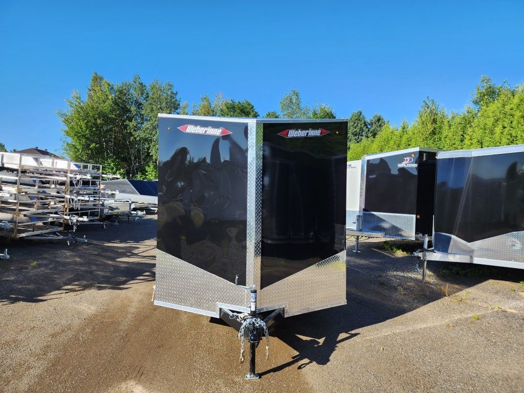 Une remorque noire et argentée est garée sur un terrain en terre.