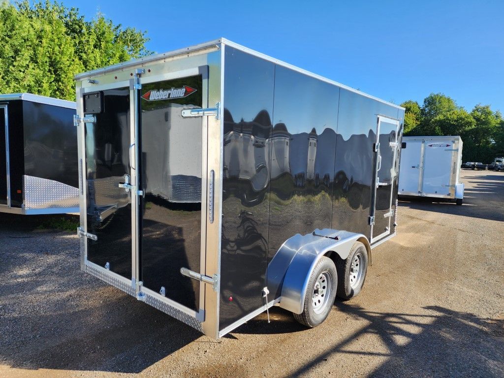 Une remorque noire et argentée est garée sur un terrain en gravier.