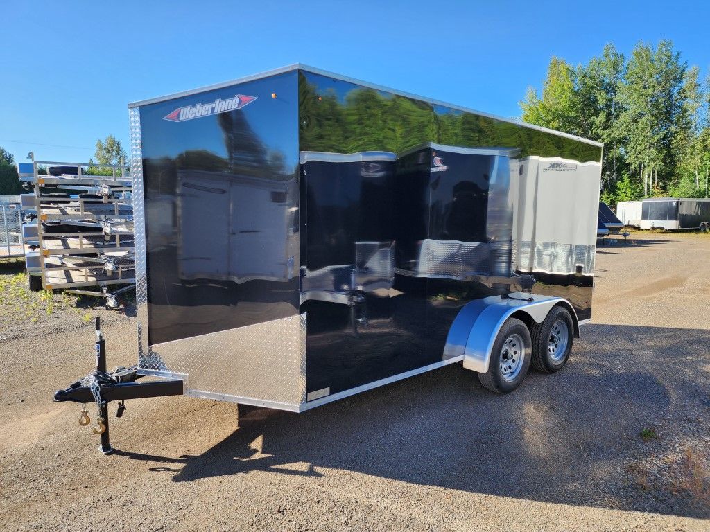 Une remorque noire est garée sur un terrain en gravier.