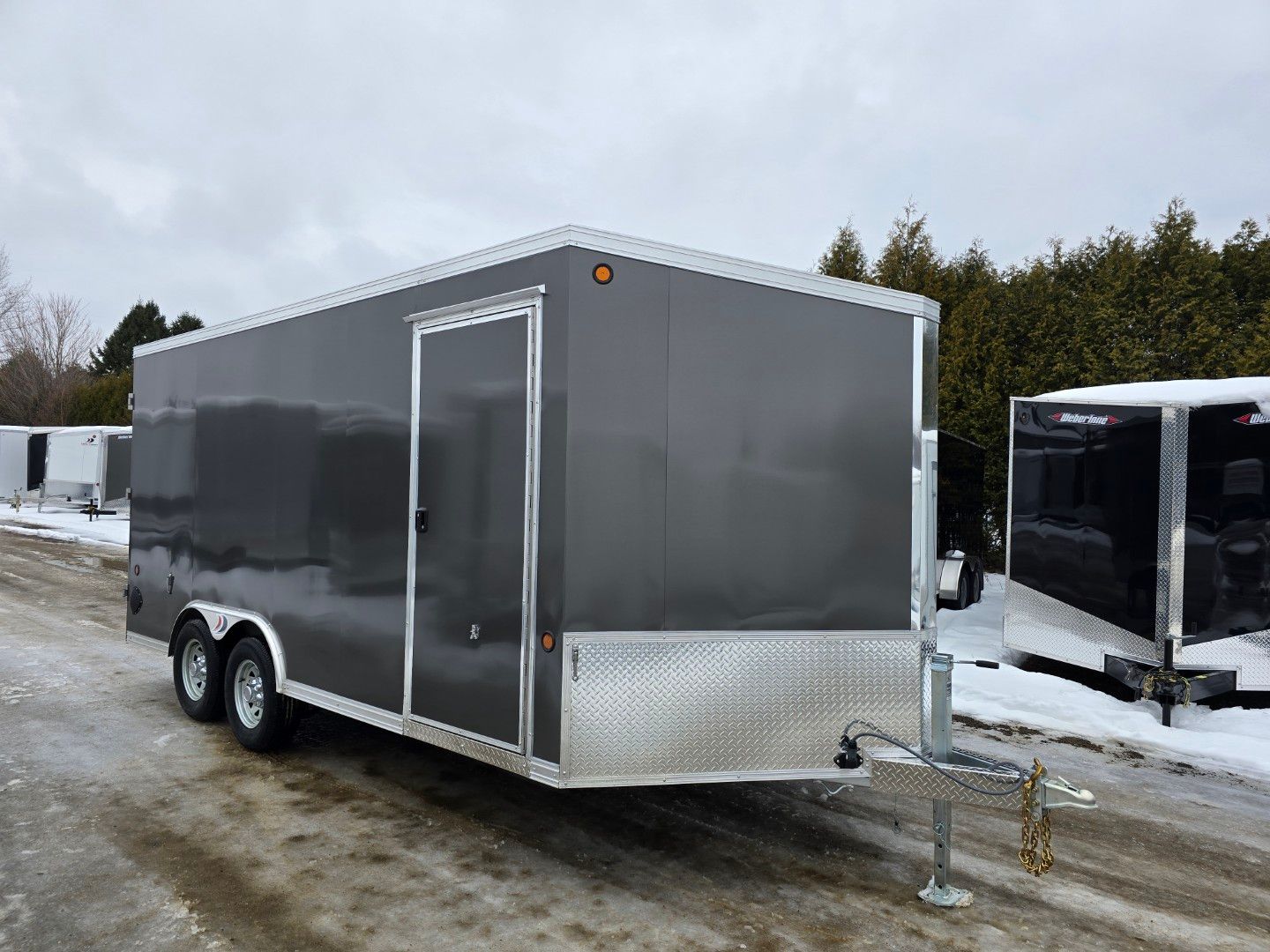 Une remorque grise est garée sur le bord d'une route enneigée.