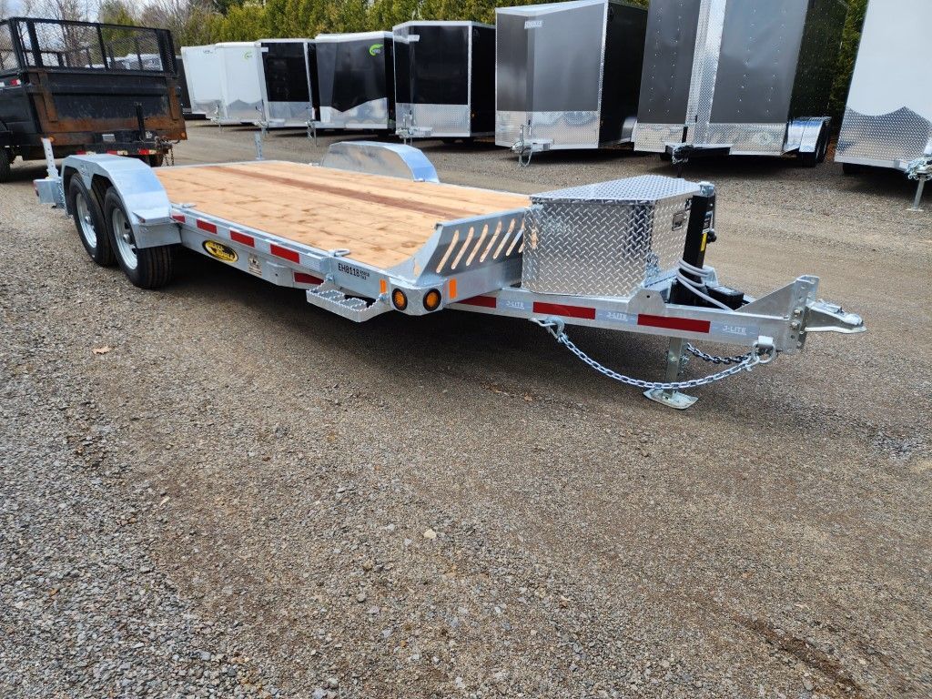 Une remorque avec une terrasse en bois est garée sur un terrain en gravier.