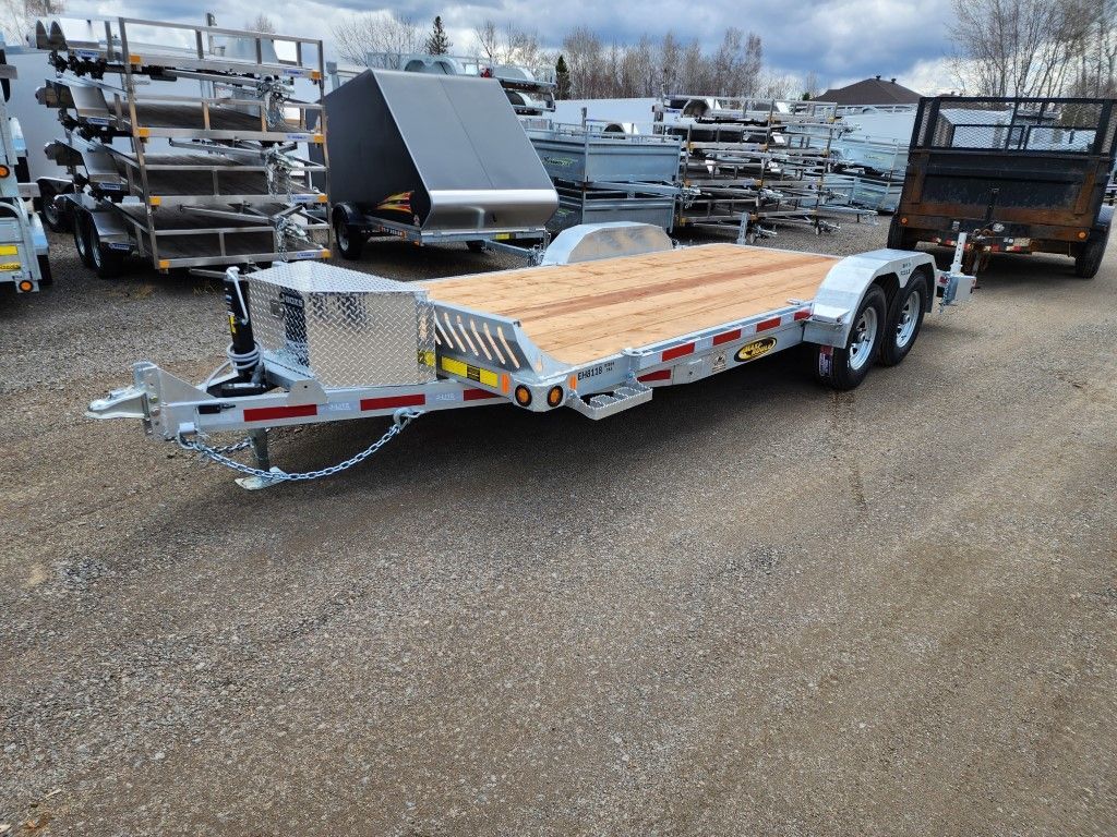 Une remorque avec une terrasse en bois est garée sur un terrain en gravier.
