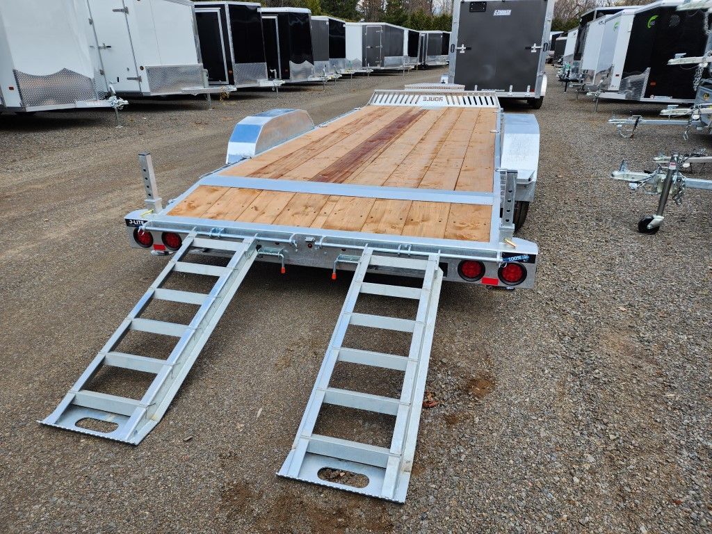Une remorque avec un pont en bois et des rampes en métal est garée dans un parking.