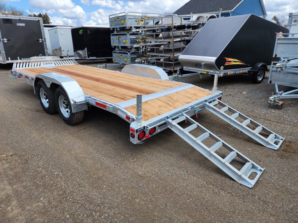 Une remorque avec un pont en bois et des rampes est garée dans un parking.