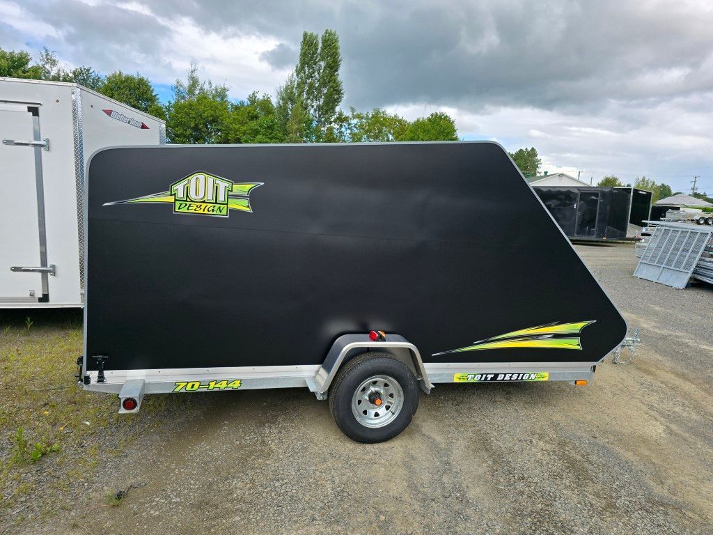 Une remorque noire est garée sur un terrain en gravier.