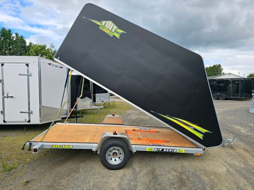 Une remorque noire avec le couvercle ouvert est garée sur un parking.