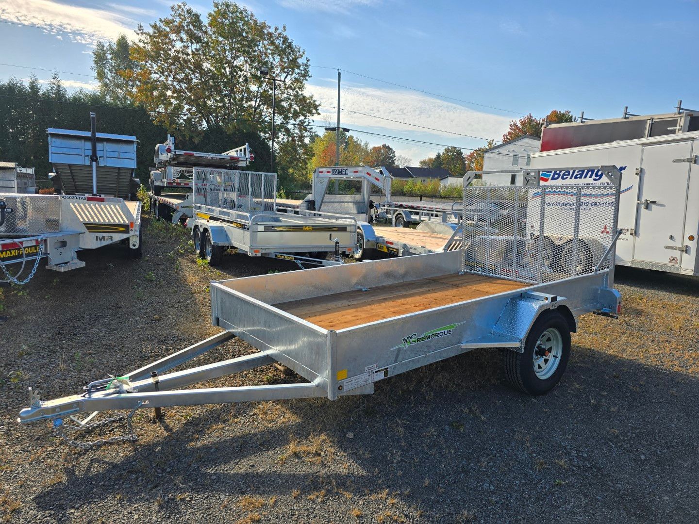 Une remorque avec une terrasse en bois est garée sur un terrain en gravier.