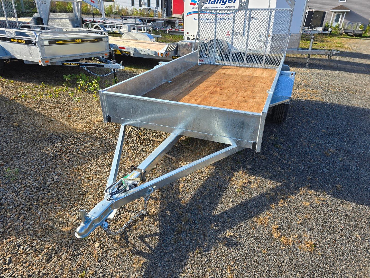 Une remorque avec une terrasse en bois est garée sur un terrain en gravier.