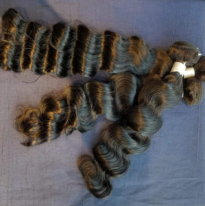 Two bundles of dark wavy hair laid out on a blue surface.