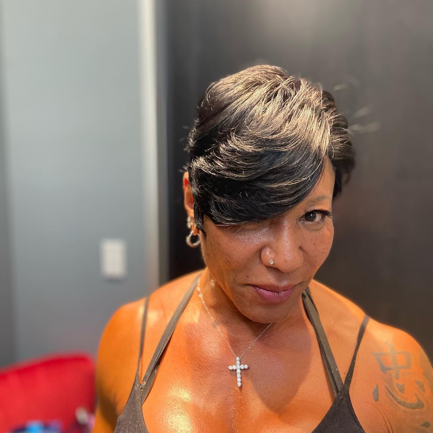 Woman with dark hair, wearing a cross necklace and black tank top, looking at the camera.