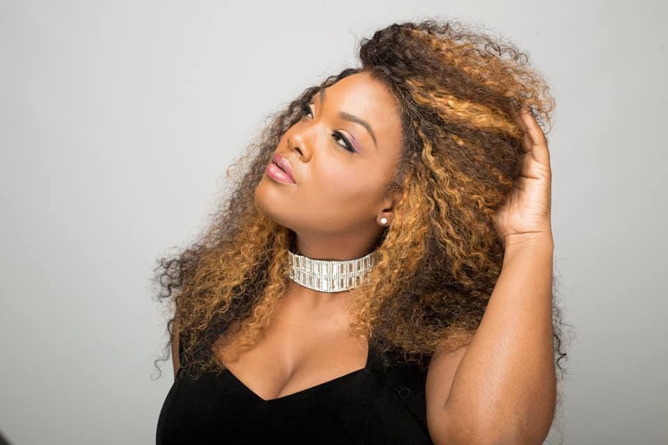 Woman with curly hair, touches her hair with a hand, and wears a choker.