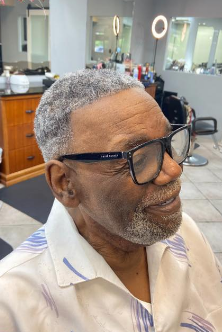 Senior man with gray hair and beard wearing glasses in a barber shop.