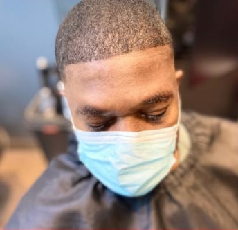 Man wearing a mask, getting a haircut. Close-up shot, with a sharp, clean hairline.