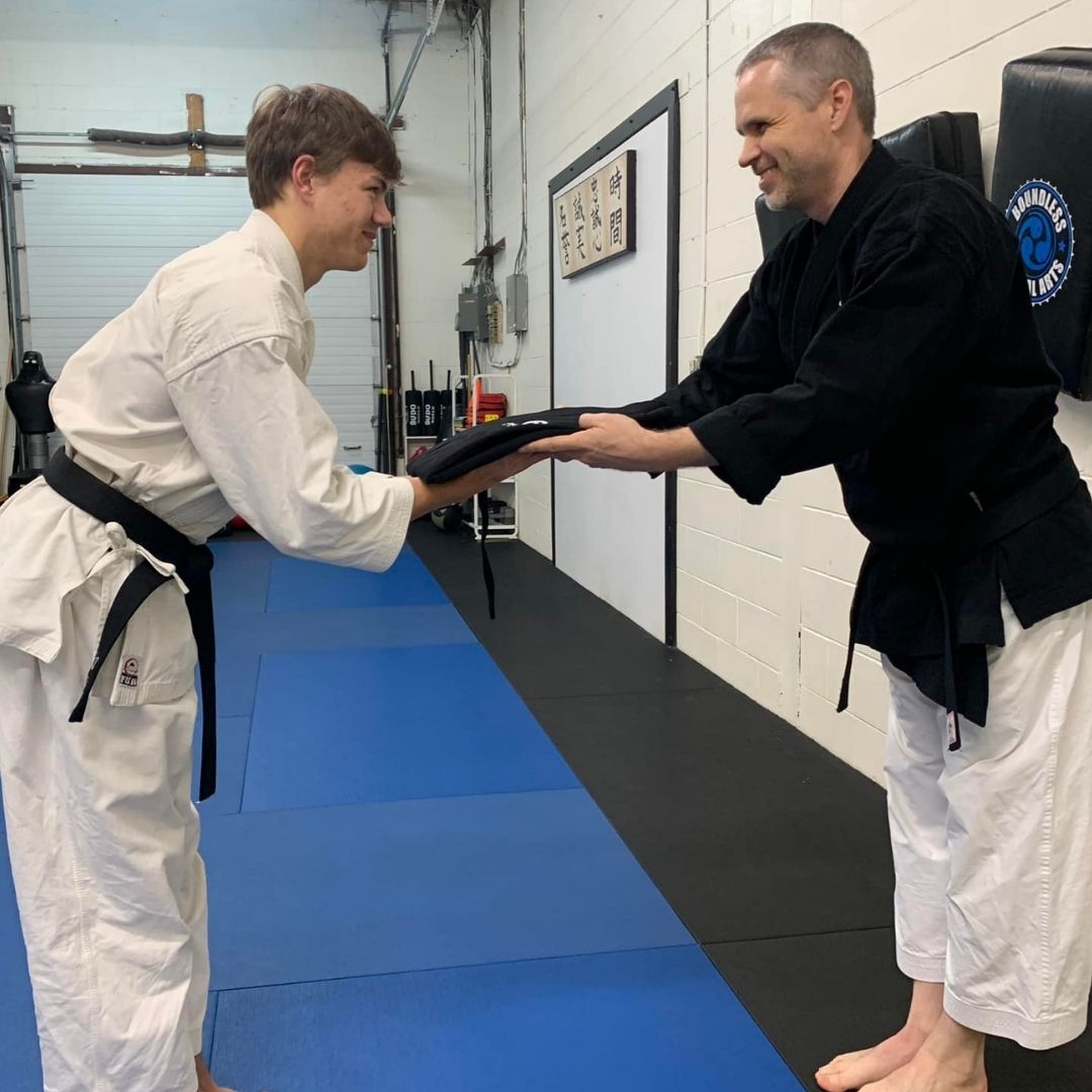 Two people practicing Brazilian Jiu-Jitsu on a mat; one in a black gi, one in a white gi, grappling.