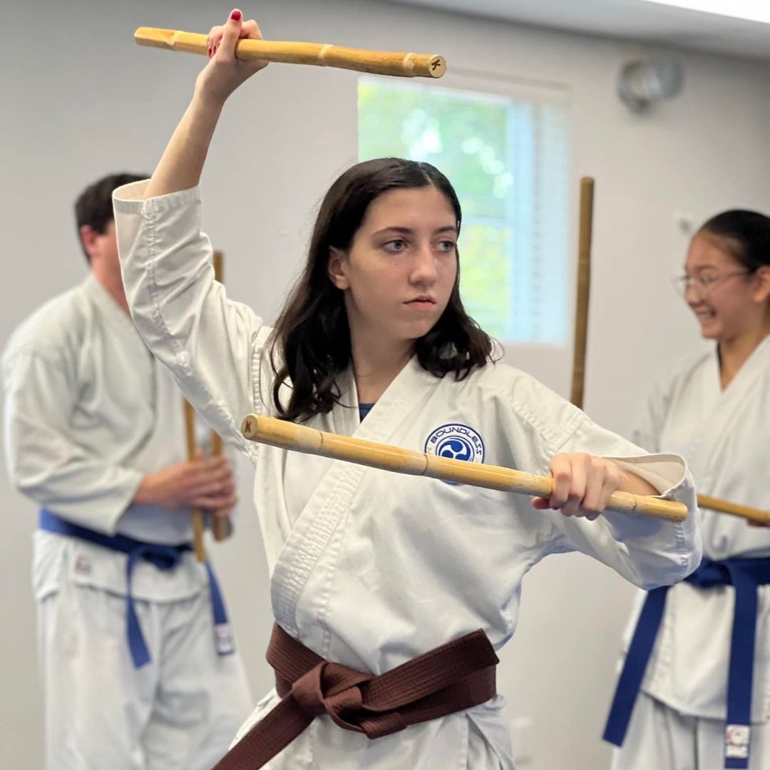 Group of children in martial arts attire posing, some with arms around each other, in a gym.