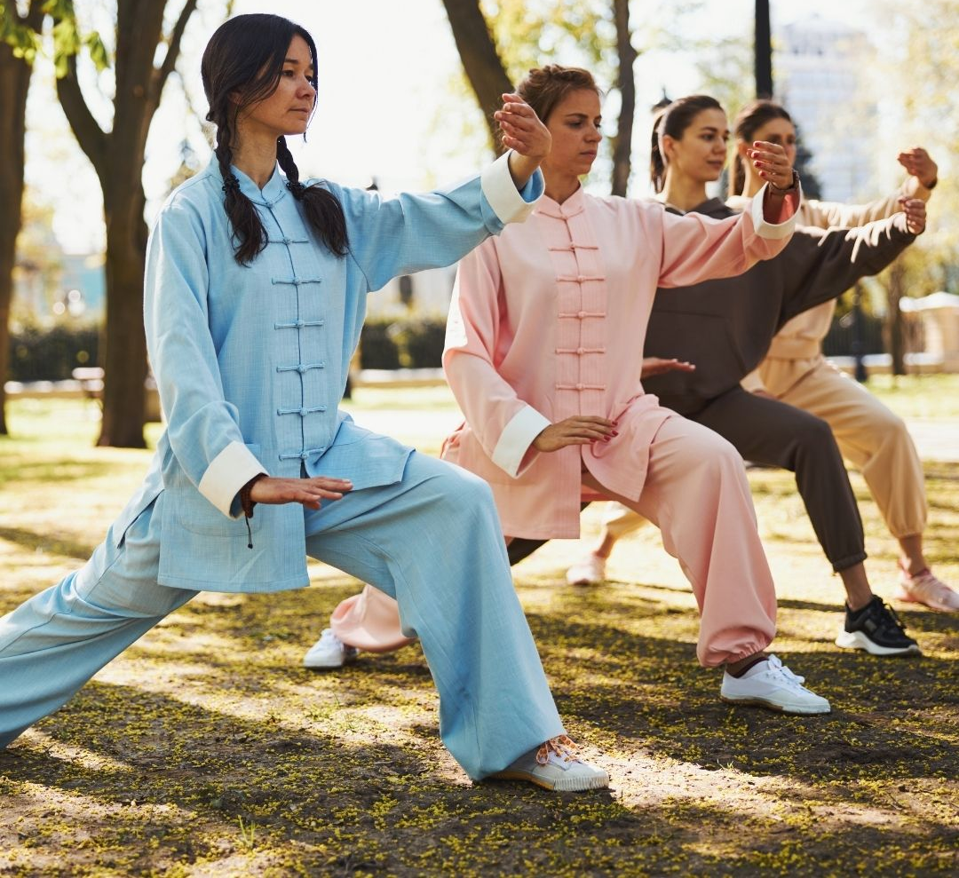 Two men in grappling position on a mat. One embraces the other from behind, both smiling. Gym setting.