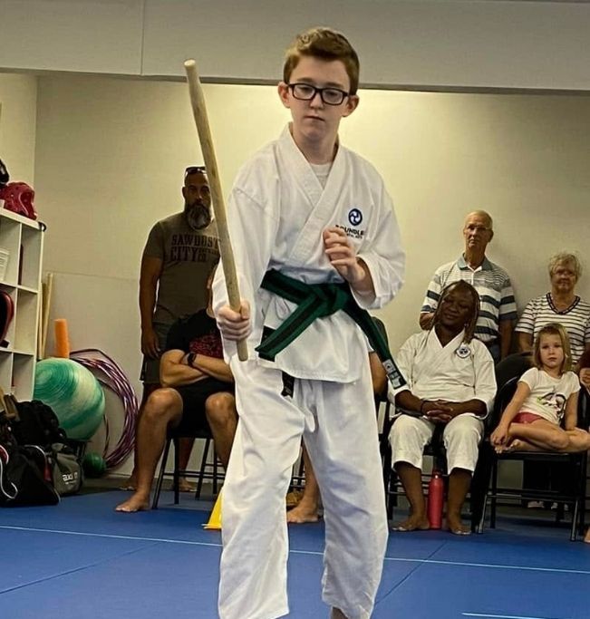 Group of children in martial arts attire posing, some with arms around each other, in a gym.