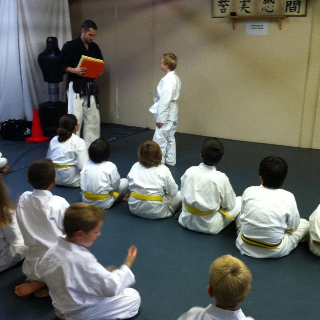 People practicing Brazilian Jiu-Jitsu. One person on the ground, another on top; two others grappling nearby. Black gis, indoor setting.