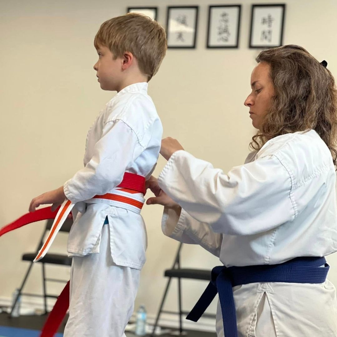 Two boys on a mat practicing Jiu-Jitsu. One boy is on top, giving a thumbs-up.