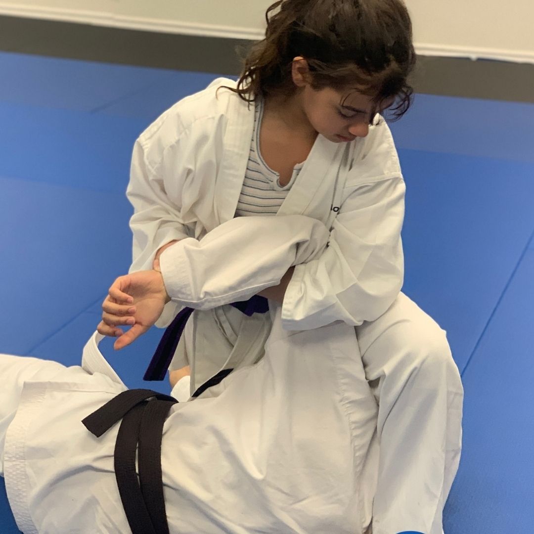 Two people practicing Brazilian Jiu-Jitsu on a mat; one in a black gi, one in a white gi, grappling.