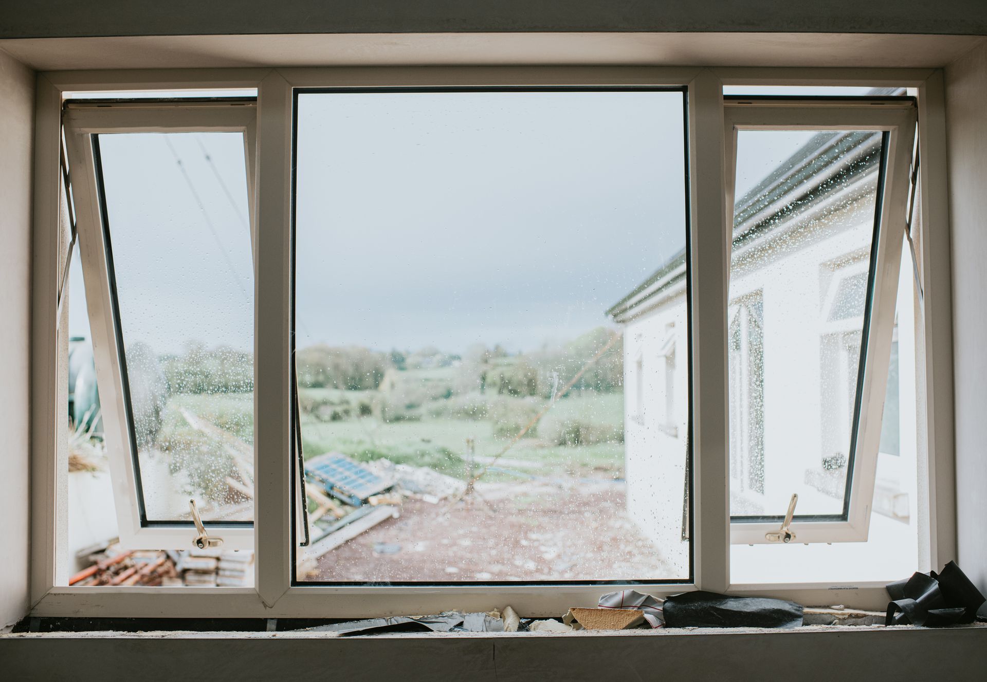 Window framing a view of a cloudy sky and a building. The window is flanked by open, white-framed windows.