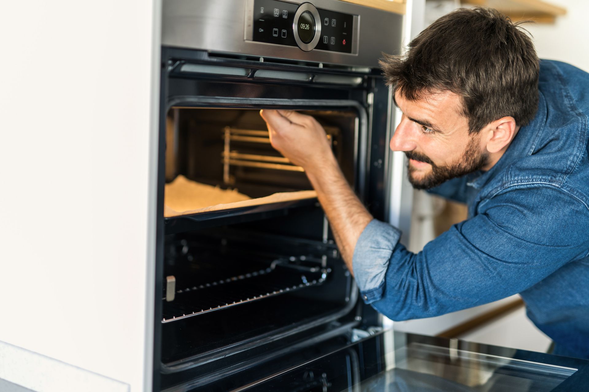 A man is opening an oven door in a kitchen.