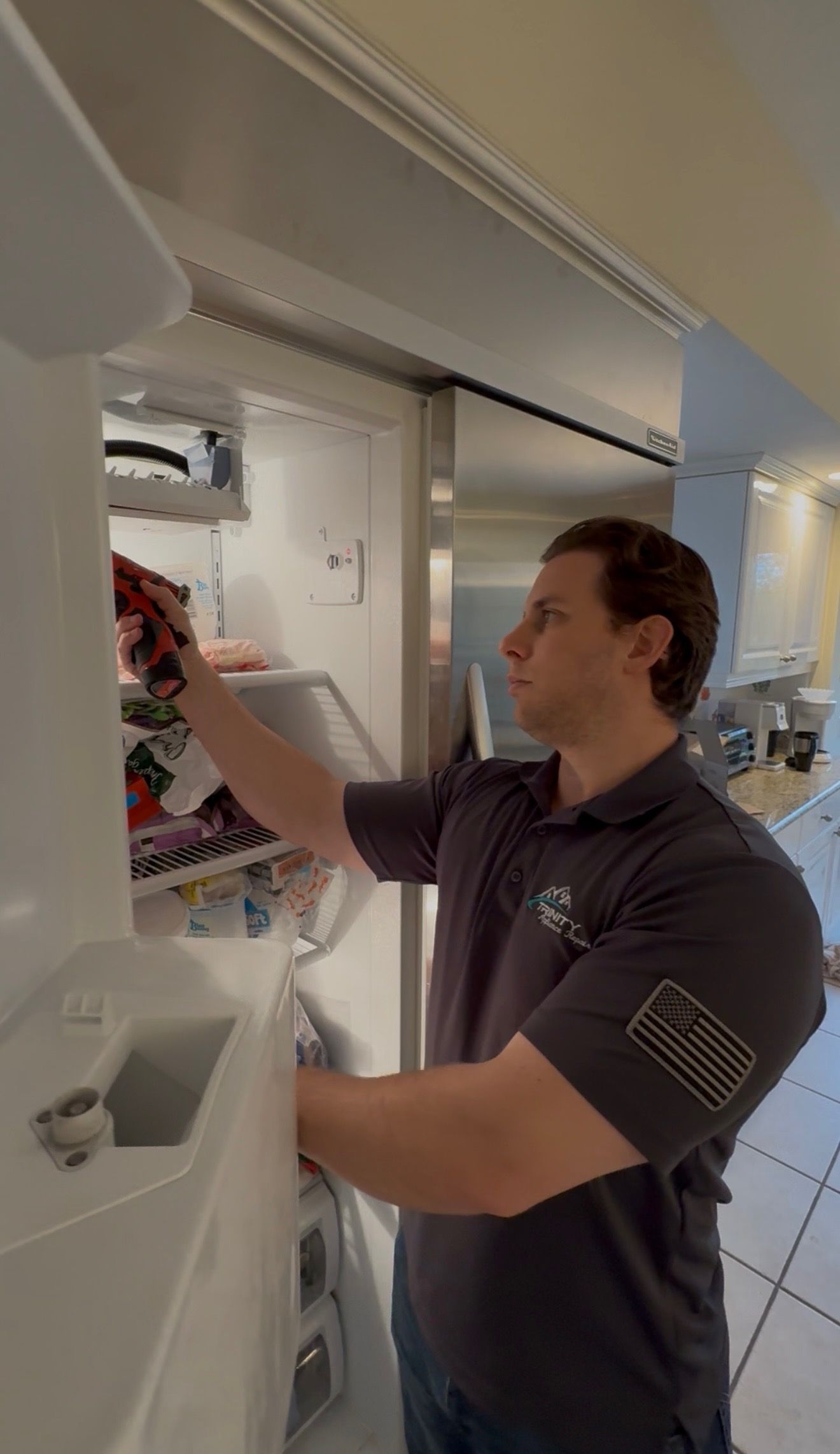A man is fixing a refrigerator with a screwdriver.