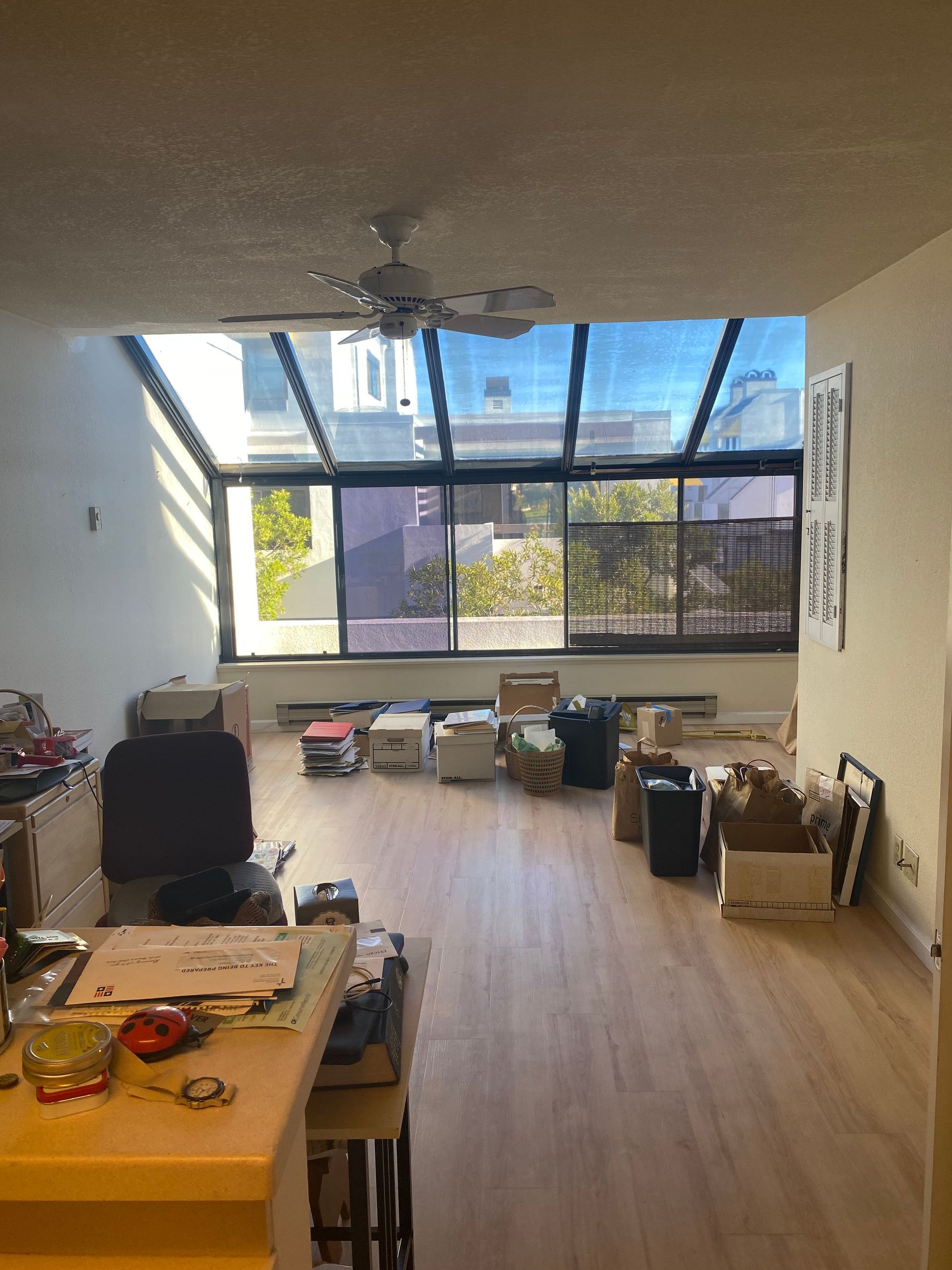 A living room with a lot of boxes on the floor and a ceiling fan.