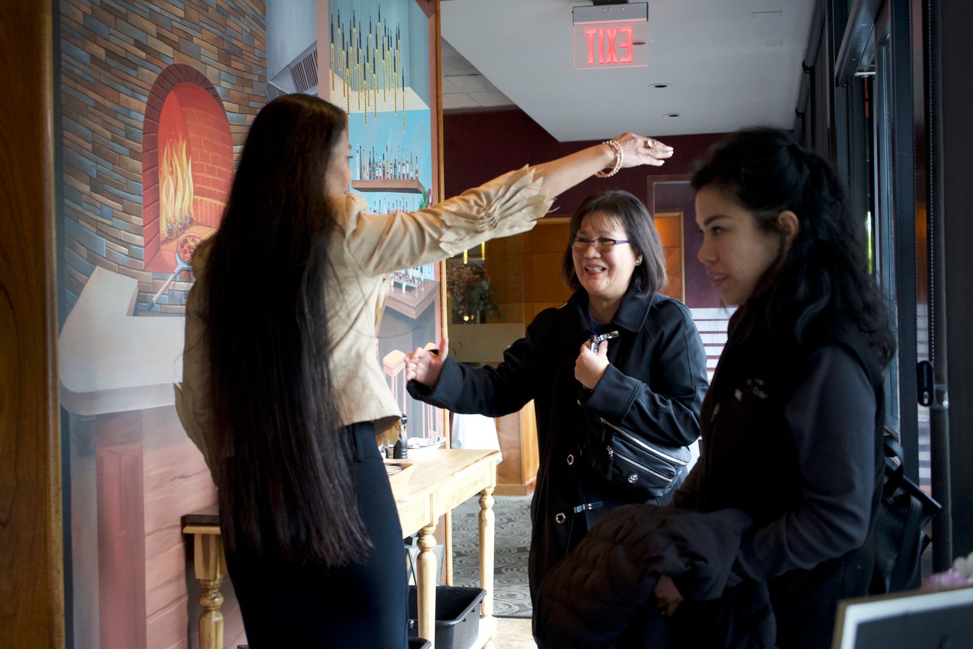 Three women are standing in front of a red exit sign