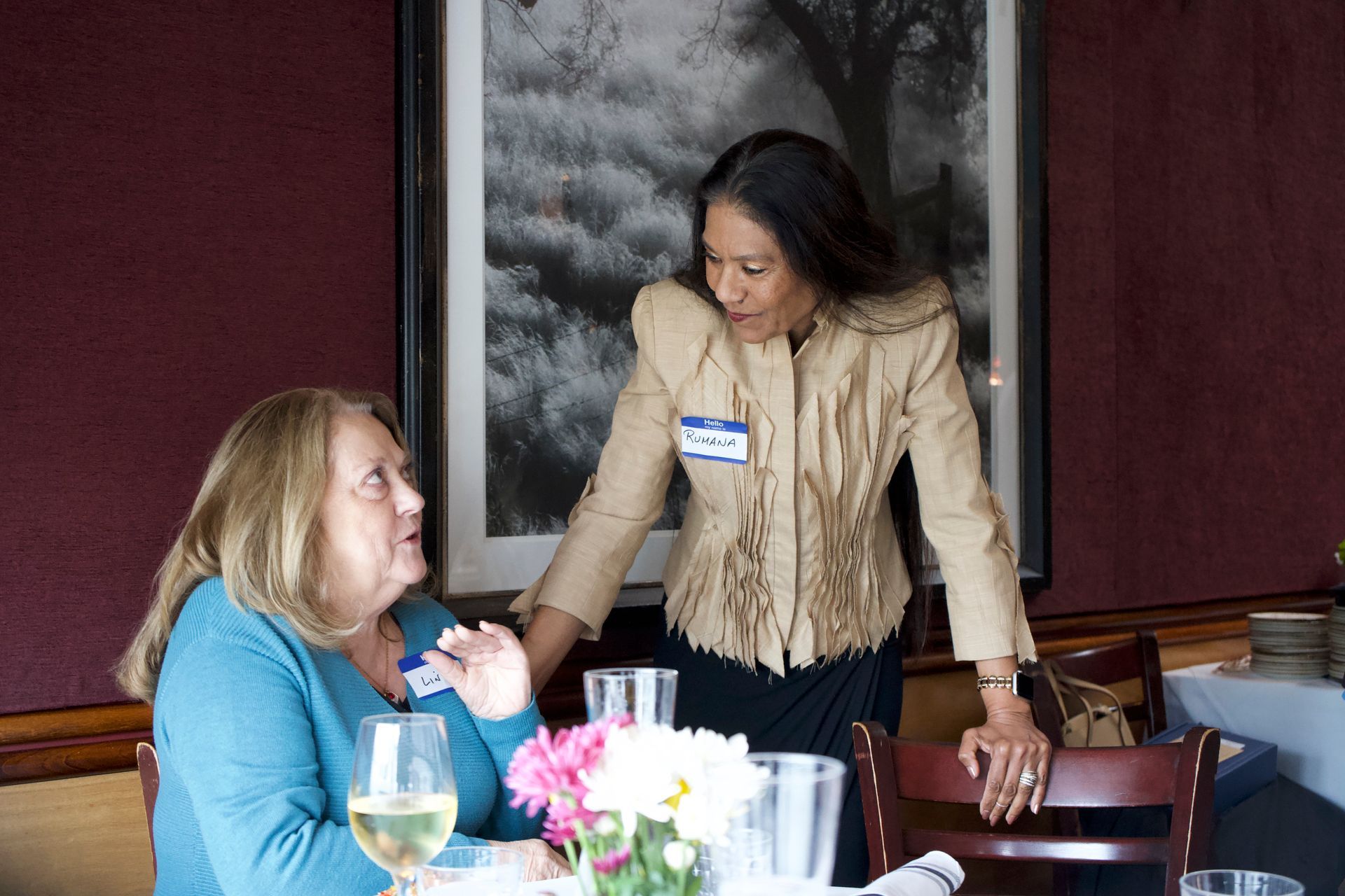 Two women are sitting at a table with glasses of wine